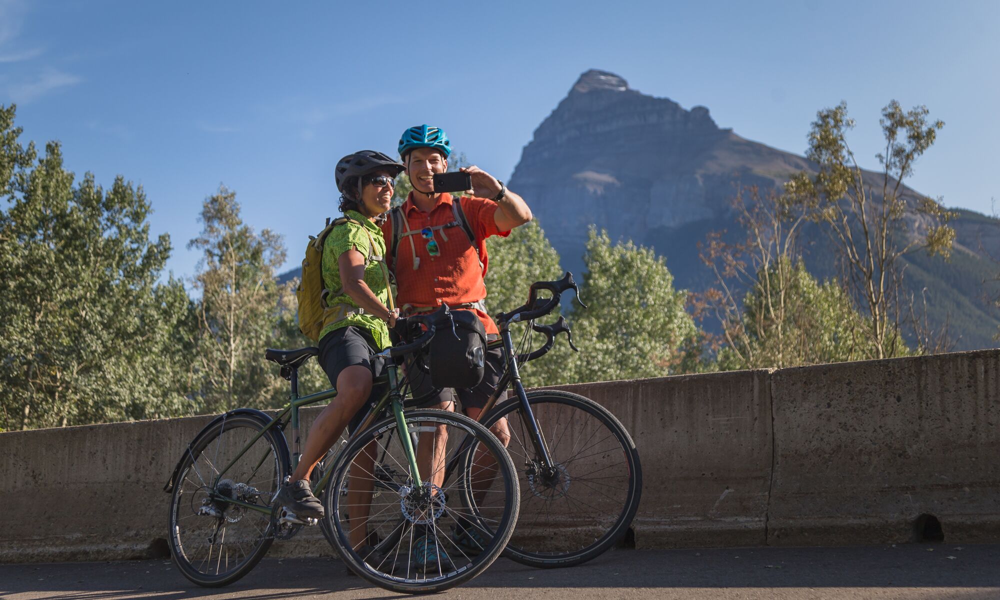 Two cyclists take a selfie while stopped on the Bow Valley Parkway in the summer.