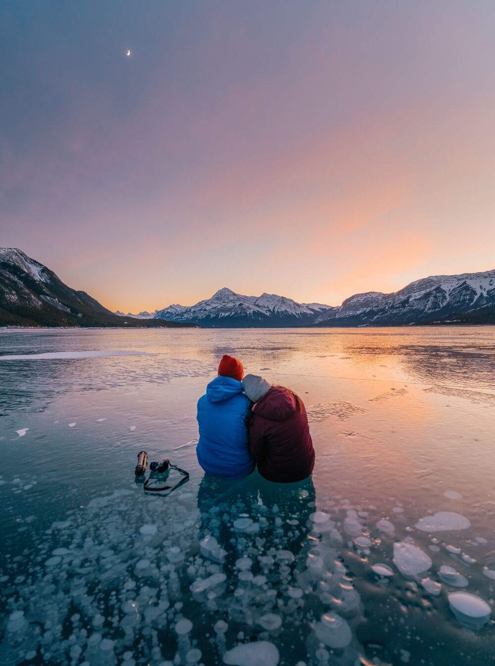 Two people sit on the ice at Abraham Lake on top of the ice bubbles in Nordegg, near Lake Louise and Banff National Park.