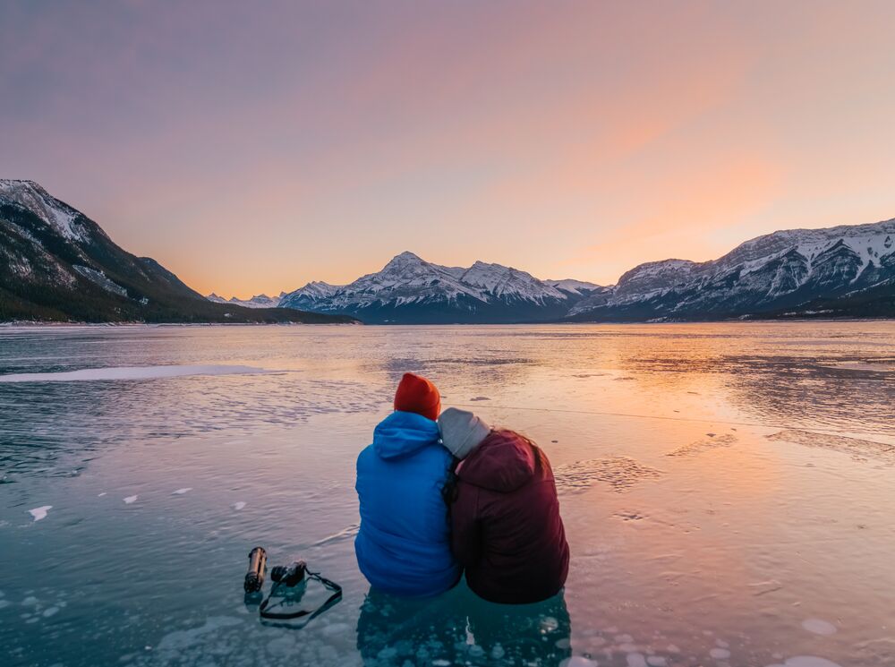Two People sitting on the frozen ice bubbles of Abraham Lake near the Icefields Parkway