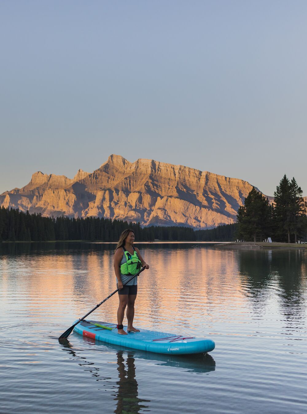 A woman paddleboards on Two Jack Lake at sunrise in Banff National Park.