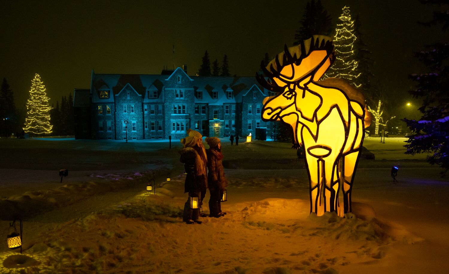A family of three stand holding lanterns in front of a winter display with a moose in Banff National Park