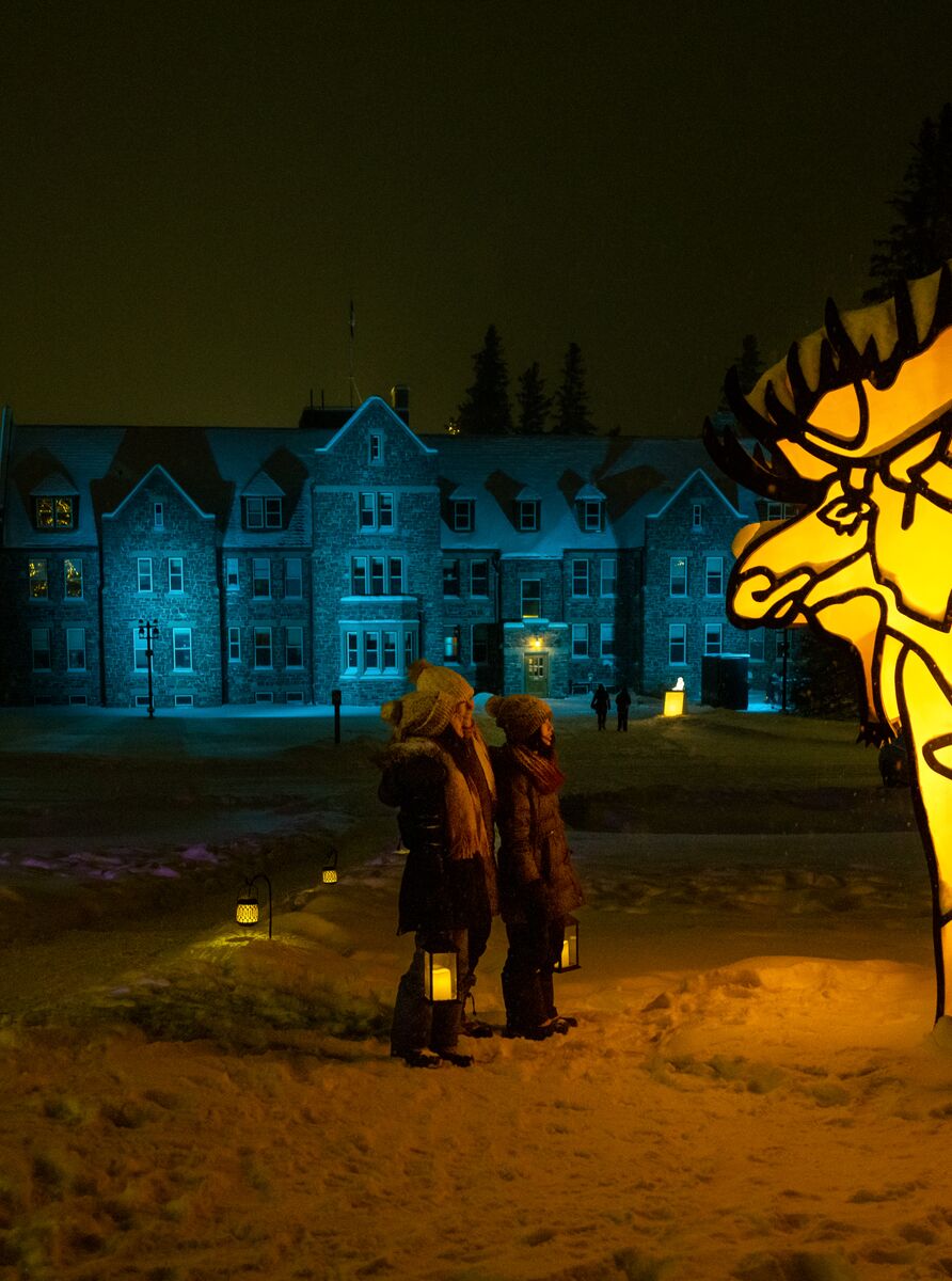 A family of three stand holding lanterns in front of a winter display with a moose in Banff National Park