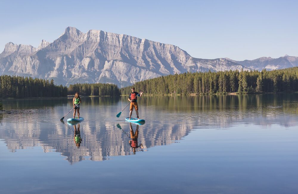 Two people stand up paddle boarding on Two Jack Lake with Mount Rundle in the background