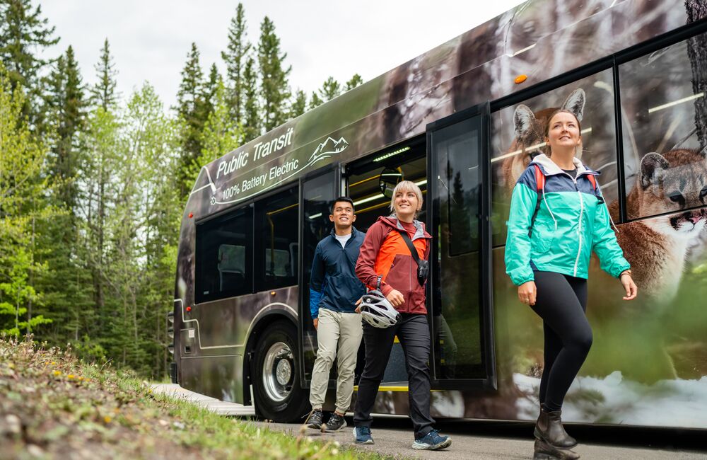 Three passengers disembark from a Roam Transit bus on the Minnewanka Loop