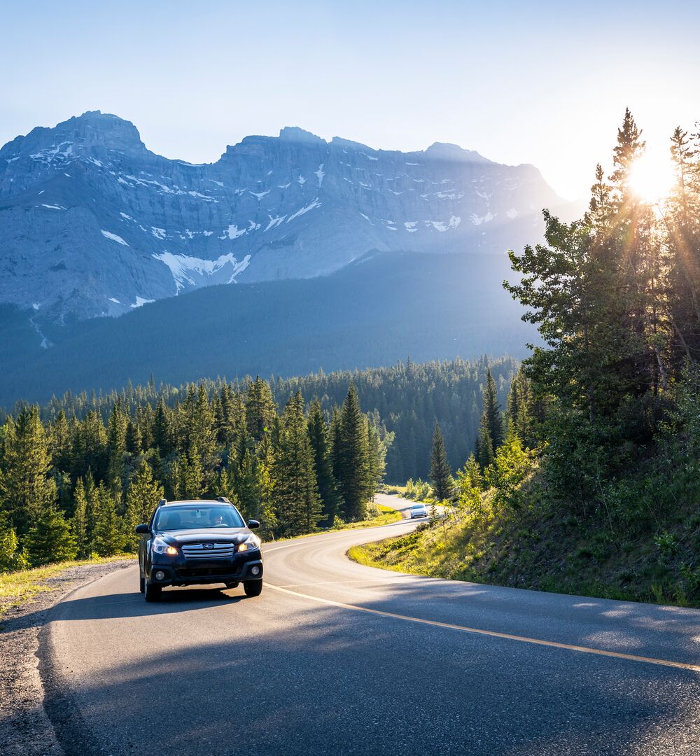 Car driving the Minnewanka Loop at sunset with Cascade Mountain in the background
