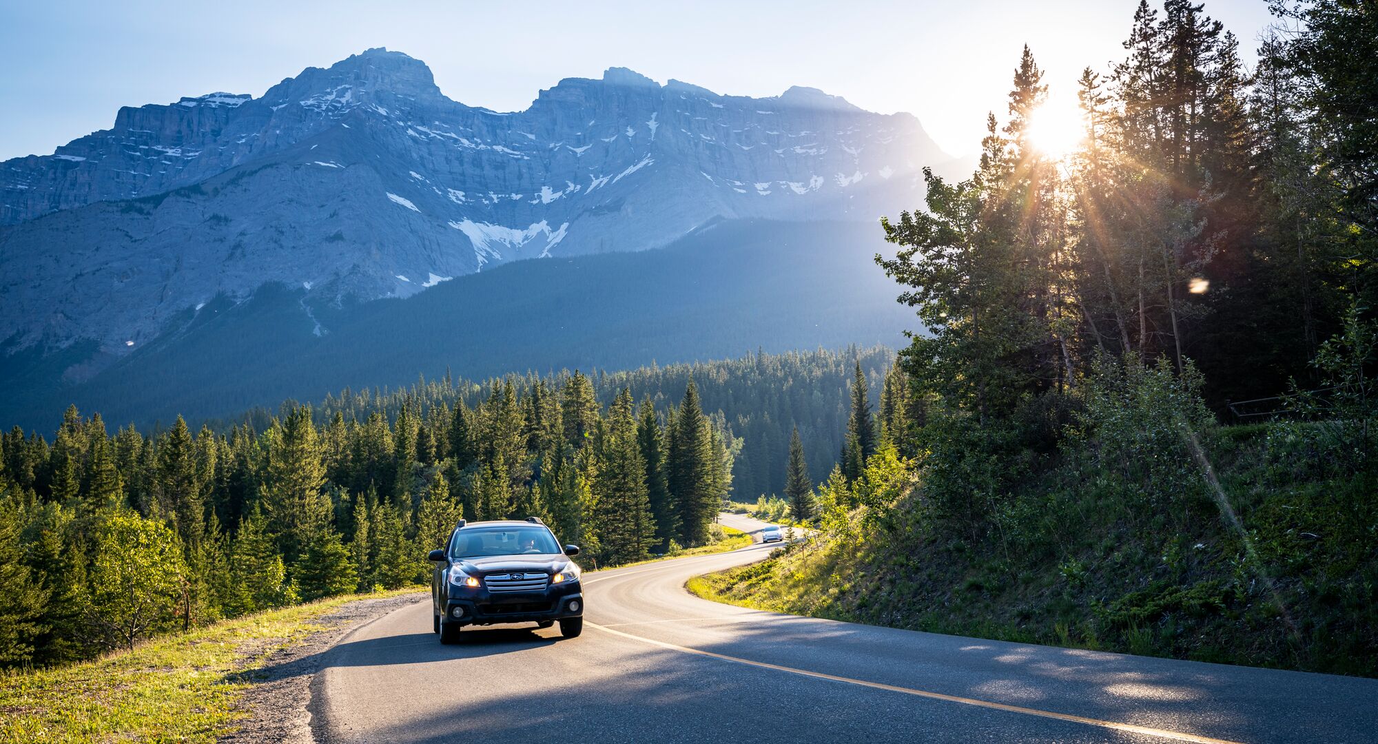 Car driving the scenic Minnewanka Loop with a mountain in the background
