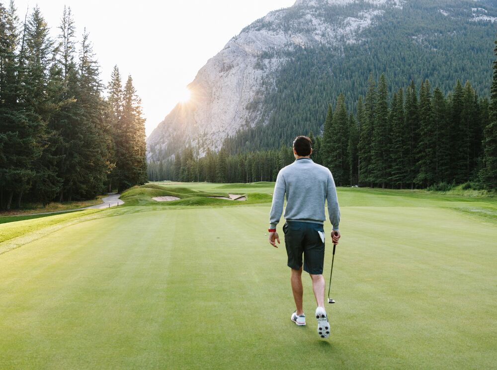 A solo golfer walks across the green at the Fairmont Banff Springs Golf Course on a sunny summer day in Banff