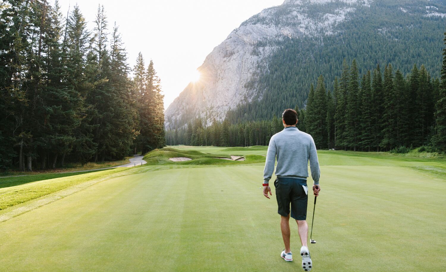 A solo golfer walks across the green at the Fairmont Banff Springs Golf Course on a sunny summer day in Banff