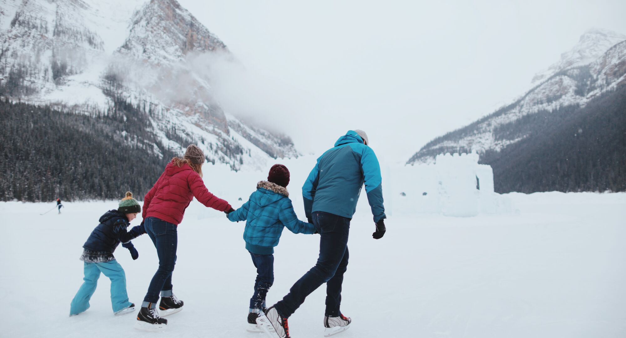 A family of four skate on frozen Lake Louise with an ice castle behind them in Banff National Park.