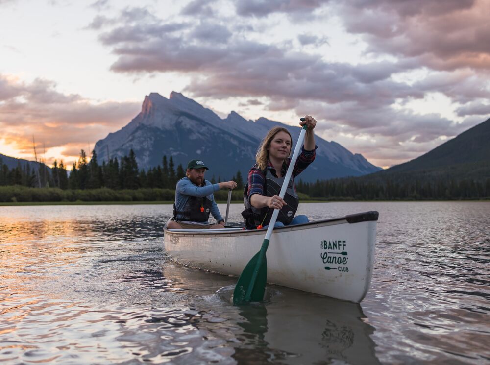 Two people canoe on Vermilion Lakes at sunrise with Mt Rundle in the background in Banff National Park.