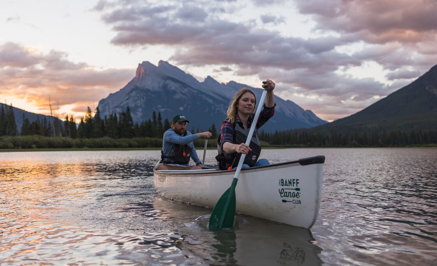 Two people canoe on Vermilion Lakes at sunrise with Mt Rundle in the background in Banff National Park.
