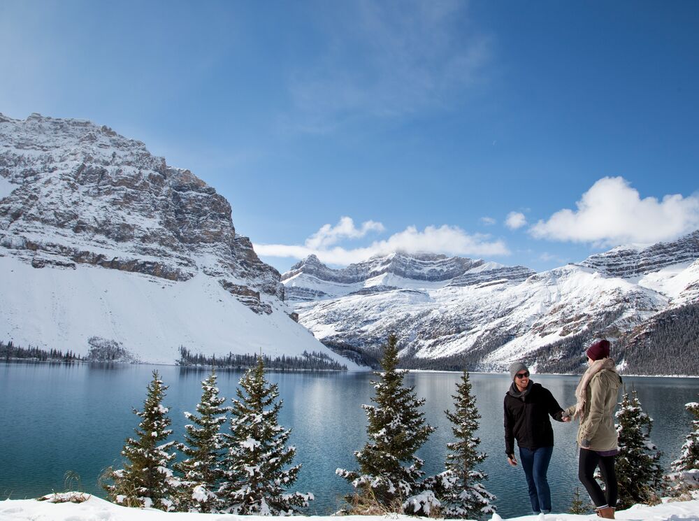 A couple walks along the edge of Bow Lake in Banff National Park.