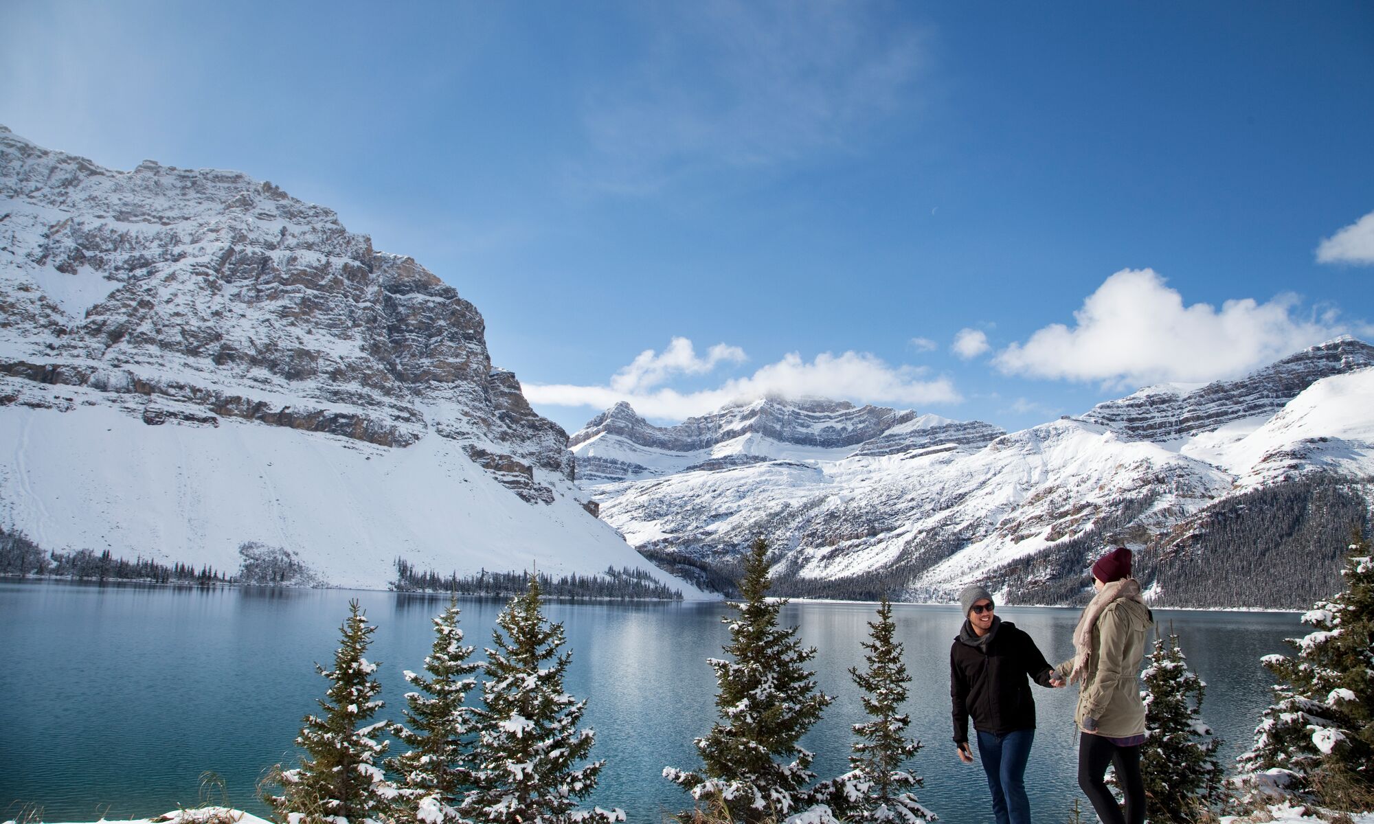 A couple walks along the edge of Bow Lake in Banff National Park.