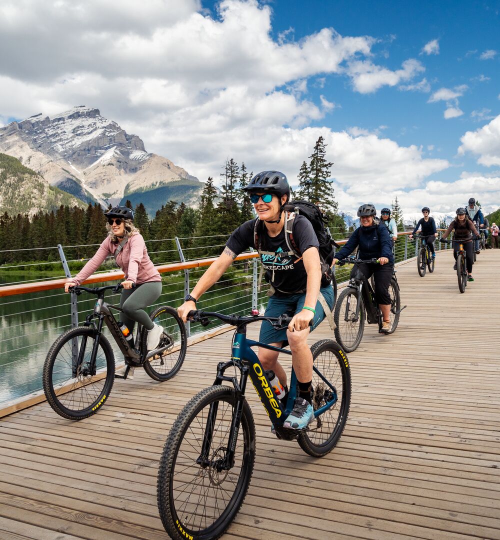 Group of people e-biking across the Banff Pedestrian Bridge