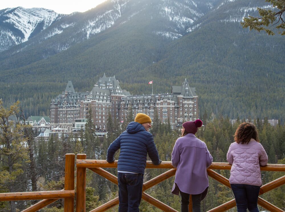 Three people at Surprise Corner viewpoint looking at the Fairmont Banff Springs in Banff National Park