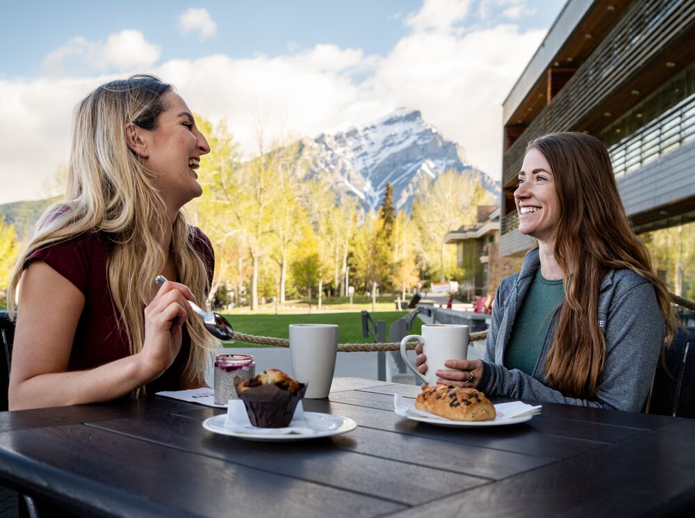 Two women have coffee and pastries at MacLab Bistro's patio at the Banff Centre for Arts and Creativity