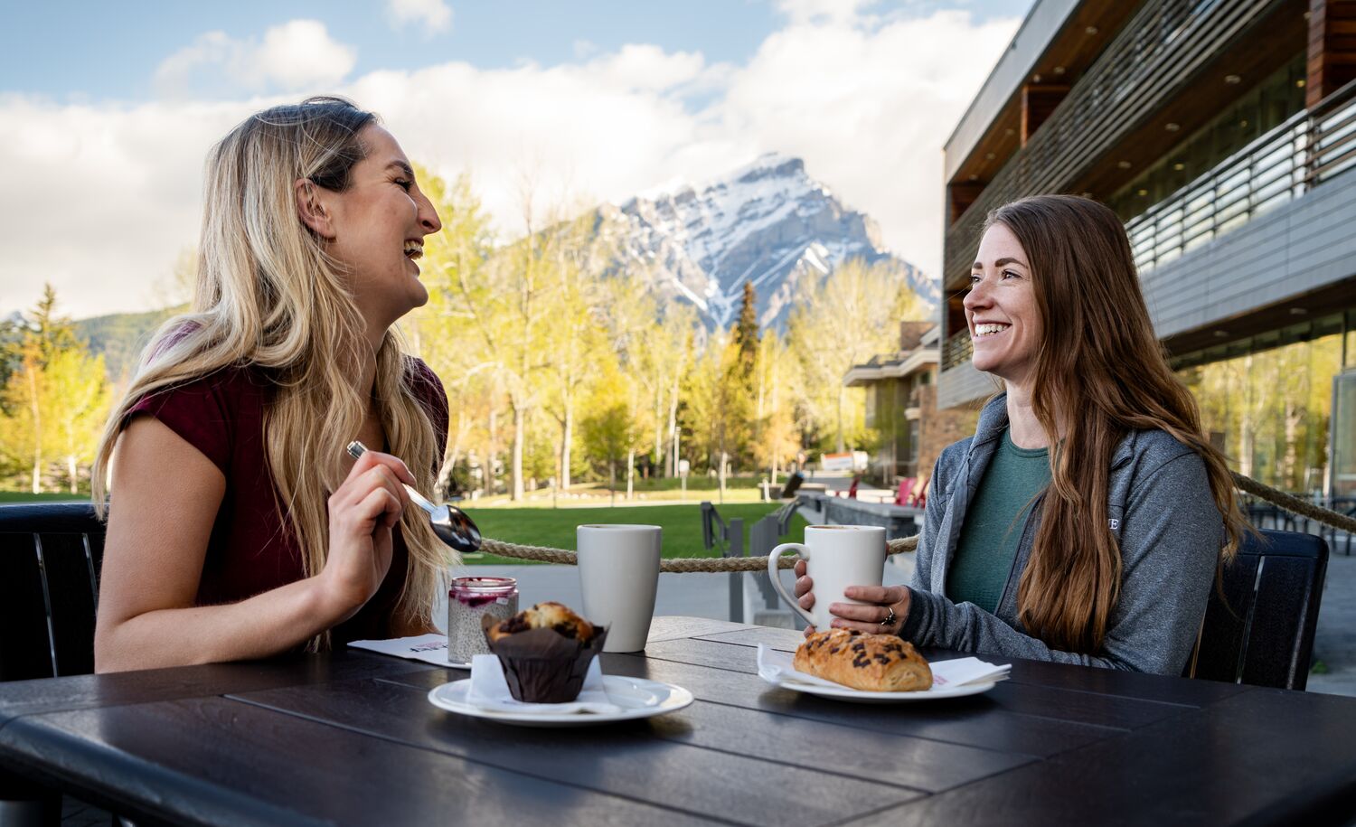 Two women have coffee and pastries at MacLab Bistro's patio at the Banff Centre for Arts and Creativity