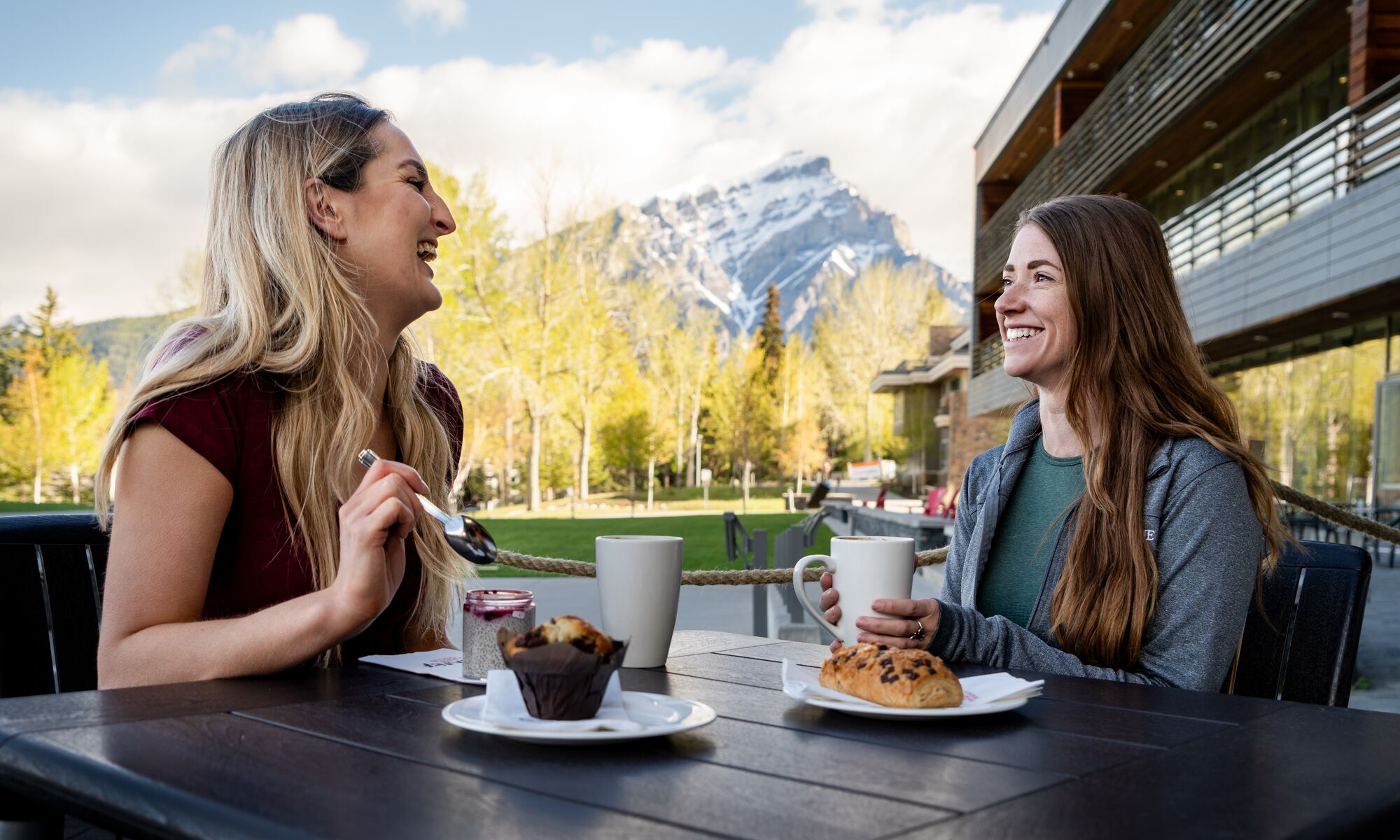 Two women have coffee and pastries at MacLab Bistro's patio at the Banff Centre for Arts and Creativity