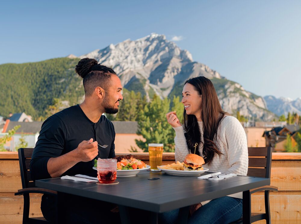 A couple enjoys cold drinks on the Rose & Crown patio in Banff on a hot summer day.
