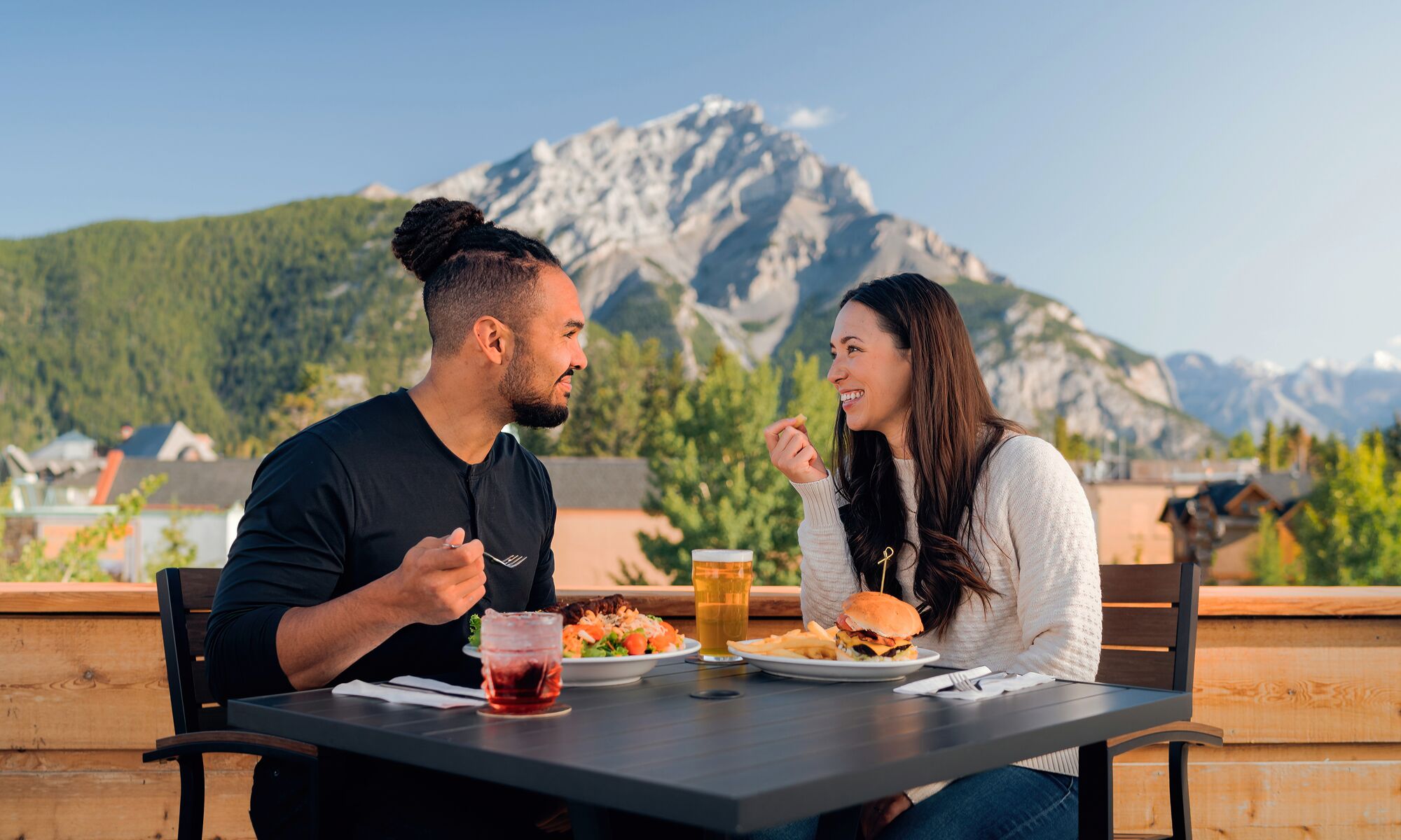 A couple enjoys cold drinks on the Rose & Crown patio in Banff on a hot summer day.