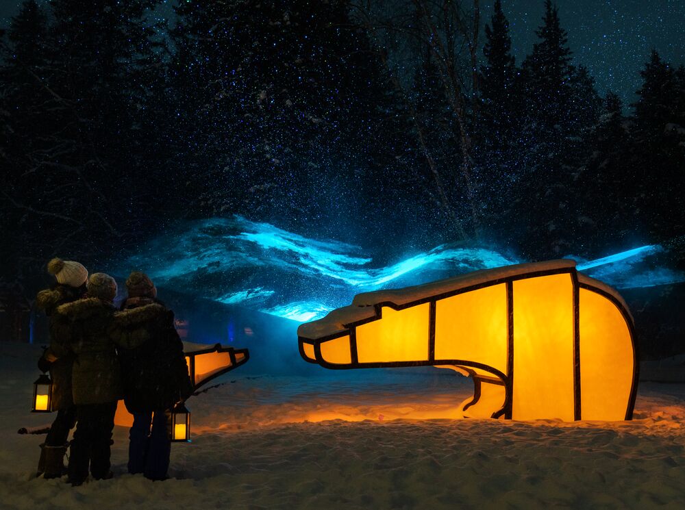 A family enjoys the In Search of Christmas Spirit event featuring light up animal sculptures on a snowy evening in Banff National Park