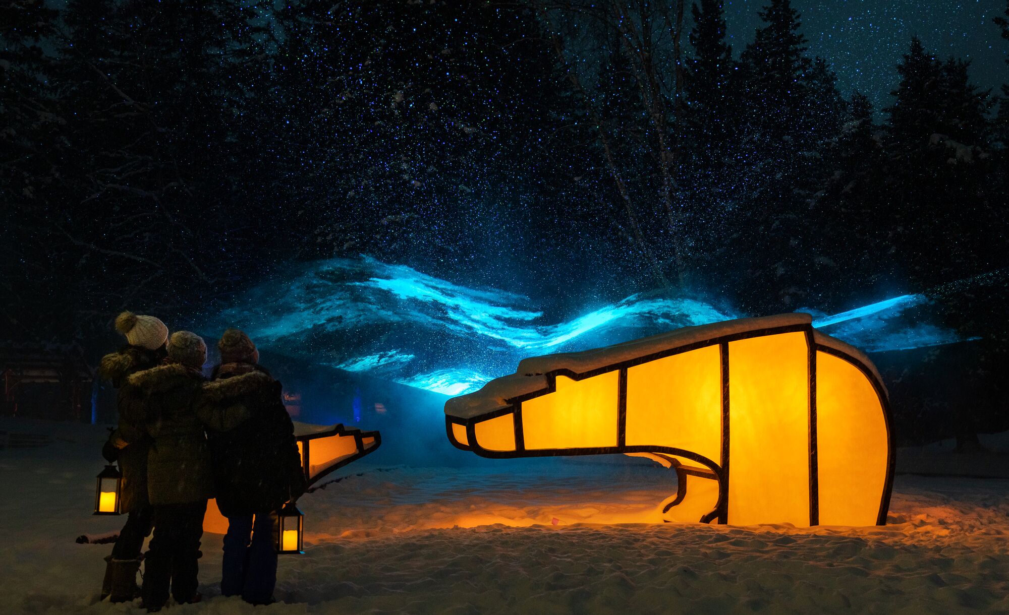 A family enjoys the In Search of Christmas Spirit event featuring light up animal sculptures on a snowy evening in Banff National Park