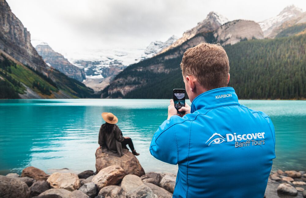A tour guide taking a photo of a guest in front of Lake Louise on a guided tour