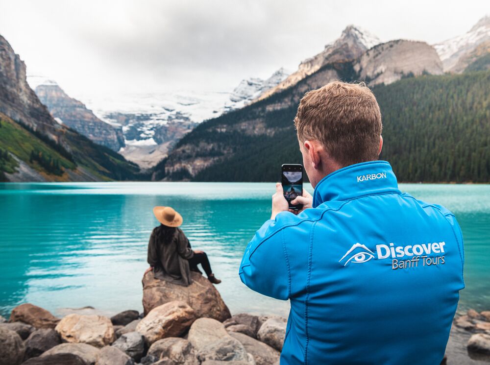 A tour guide taking a photo of a guest in front of Lake Louise on a guided tour
