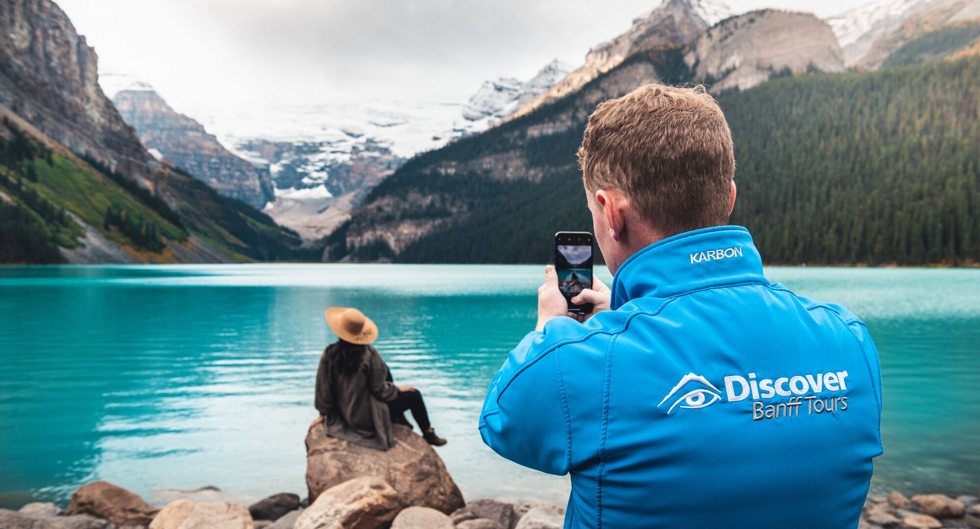 A tour guide taking a photo of a guest in front of Lake Louise on a guided tour