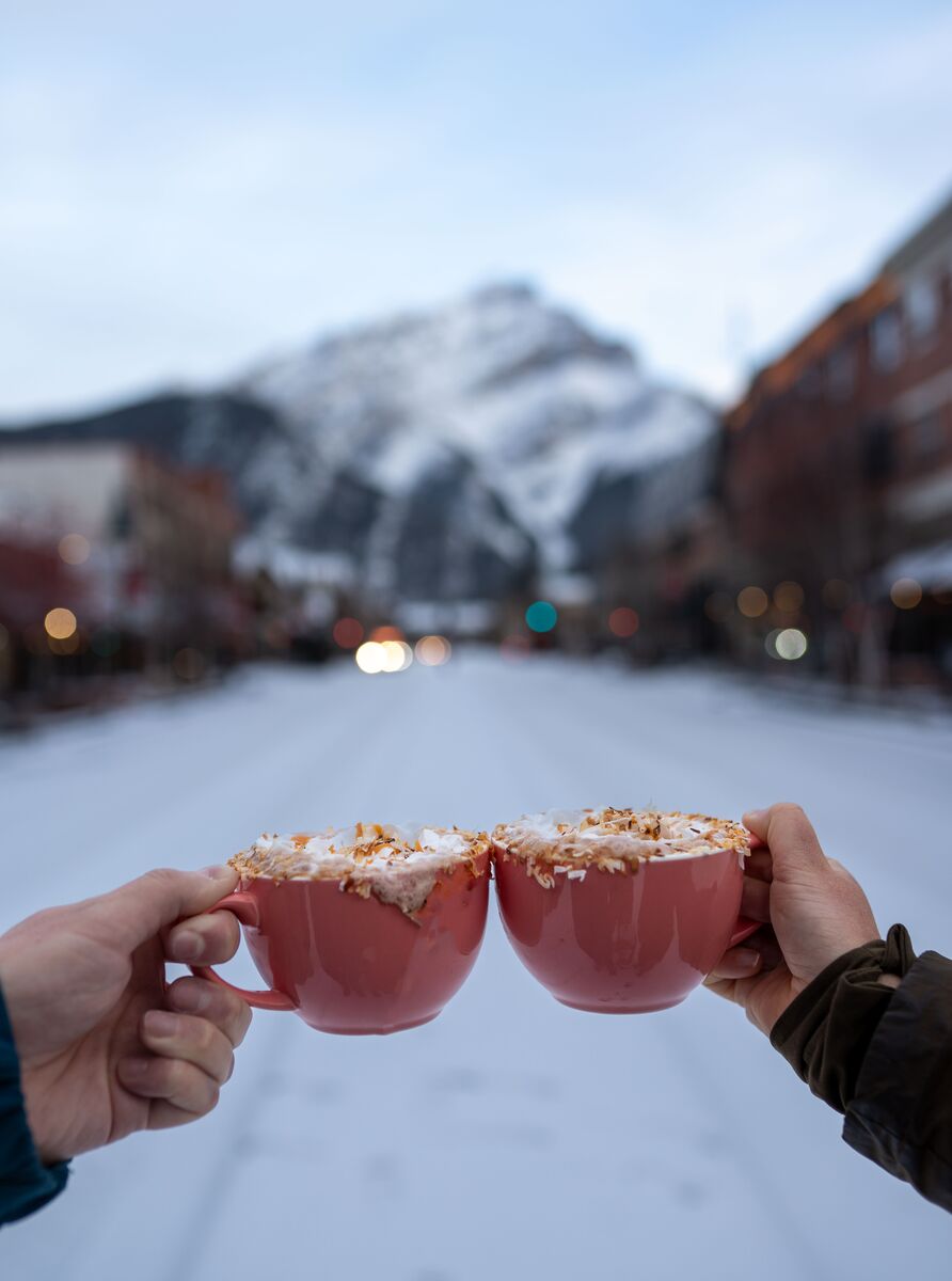 Two hot chocolates on Banff Avenue with Cascade Mountain in the background as part of Banff's Hot Chocolate Trail.