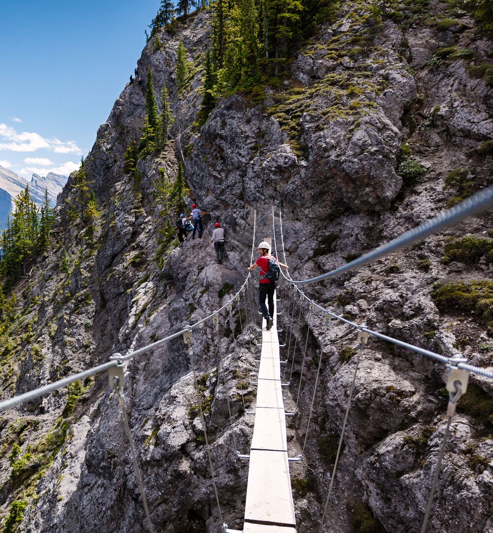 A person crossing a wooden suspension bridge at the Mt. Norquay Via Ferrata