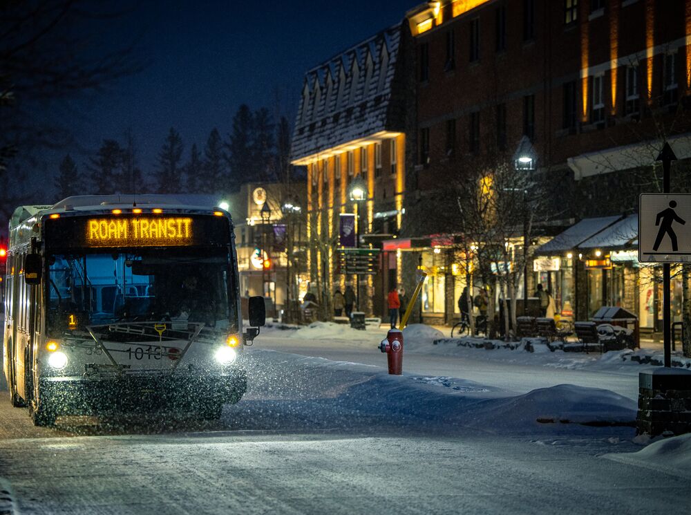 A Roam Transit bus travels down Banff Avenue on a snowy evening