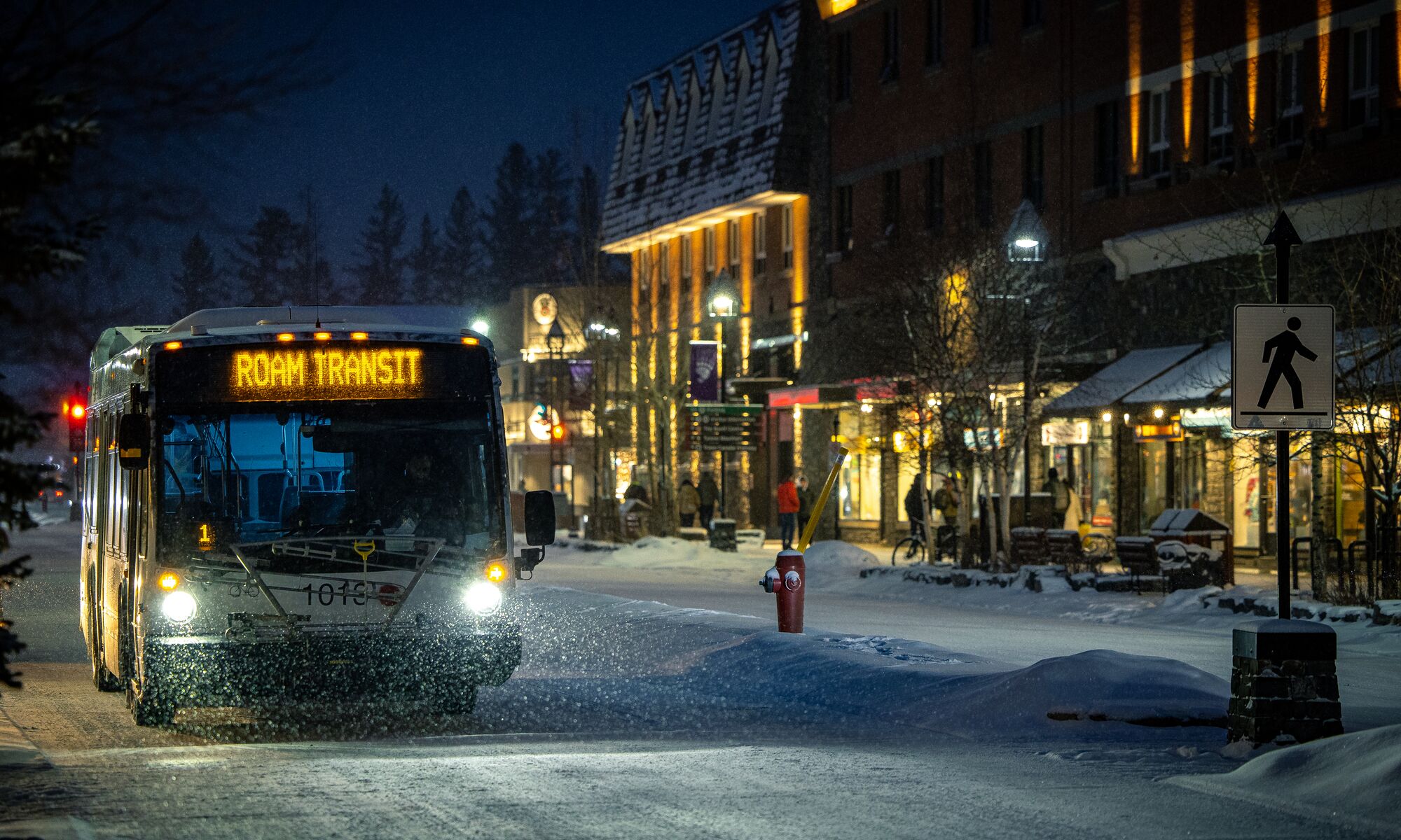 A Roam Transit bus travels down Banff Avenue on a snowy evening
