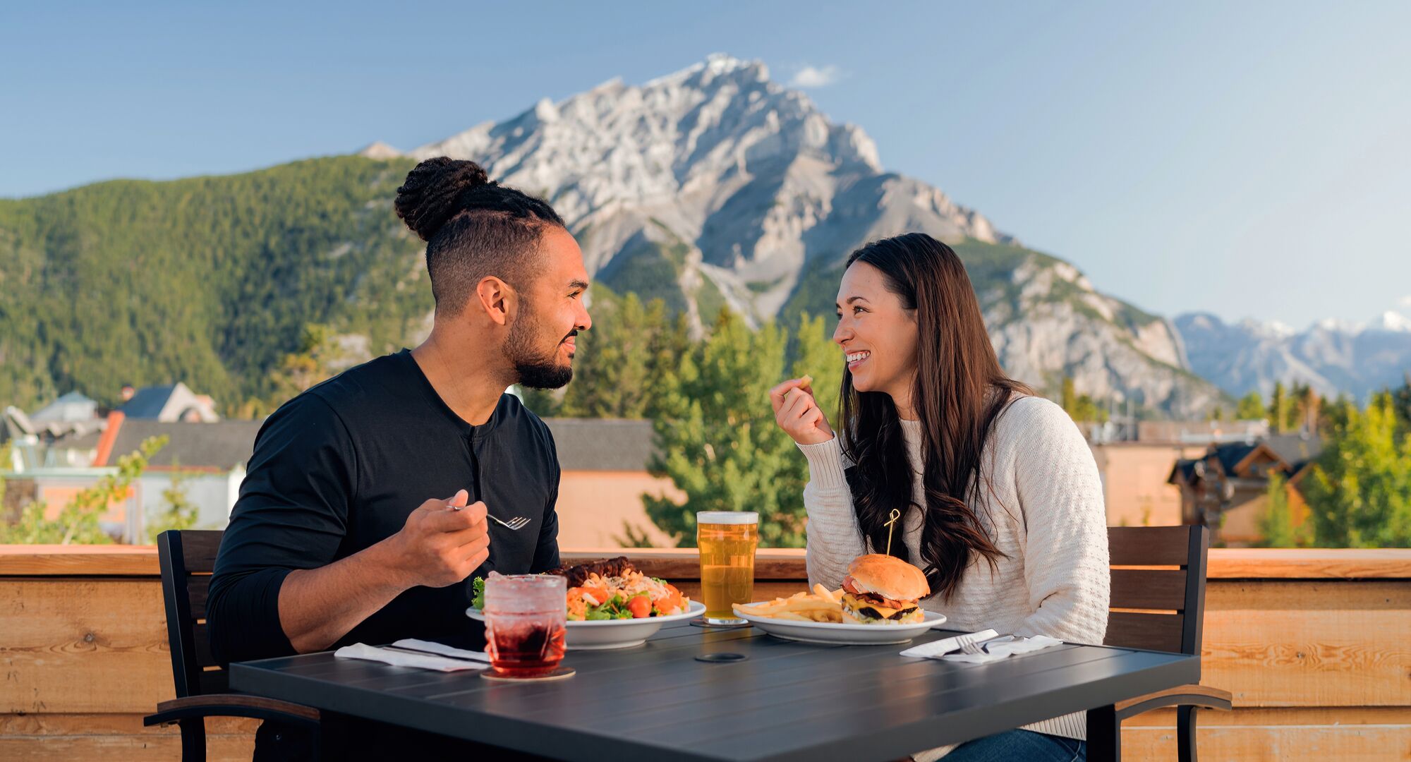 A couple enjoying a meal on a roof top patio in the summer time in Banff