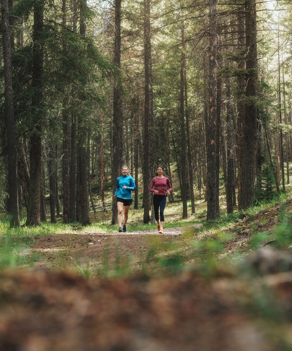 Two people trail running through a forest in Banff National Park.