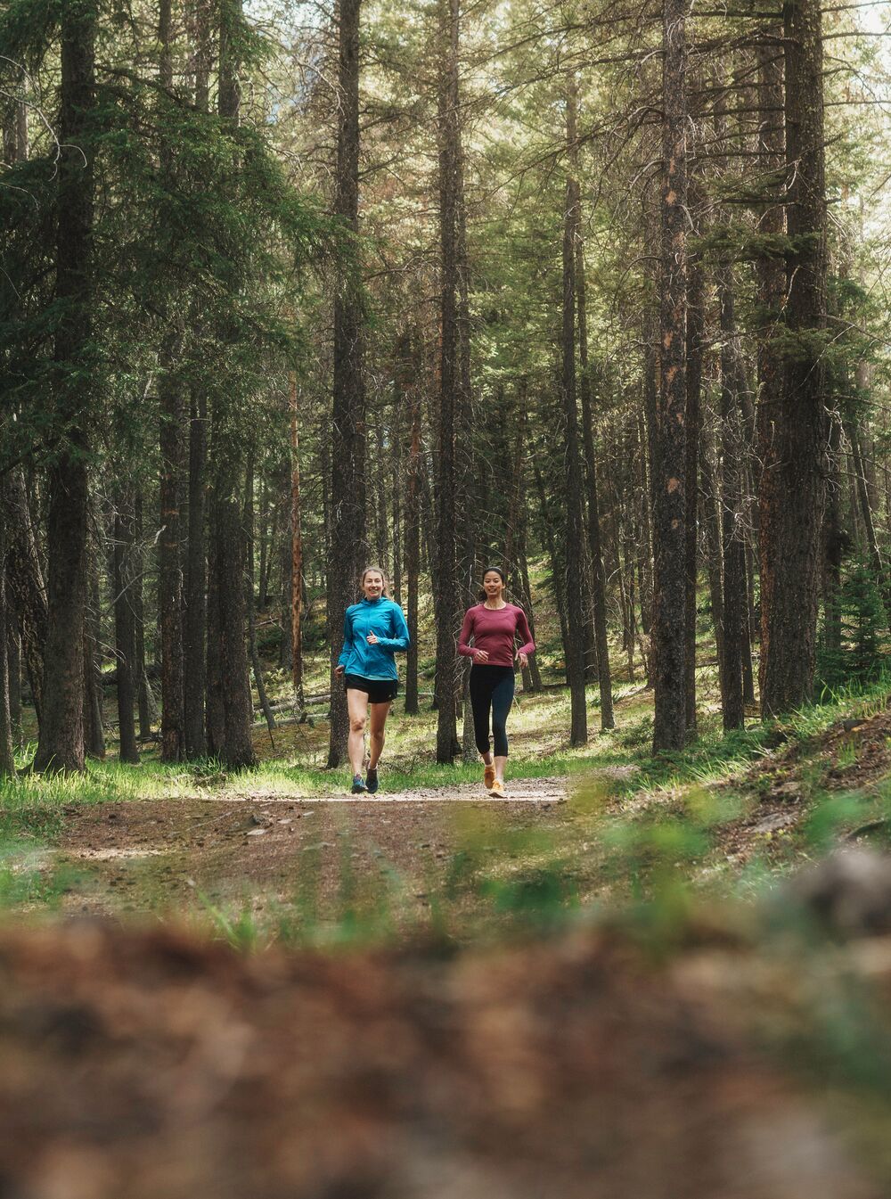 Two people trail running through a forest in Banff National Park.