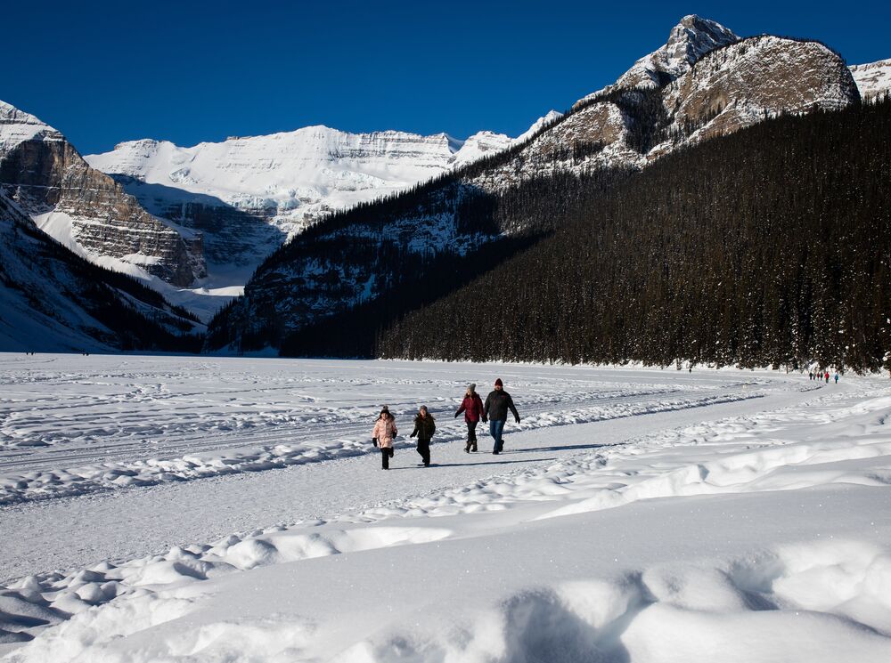 A family walks on the snow on the Lake Louise Lakeshore trail - one of Banff's best hikes in the winter.