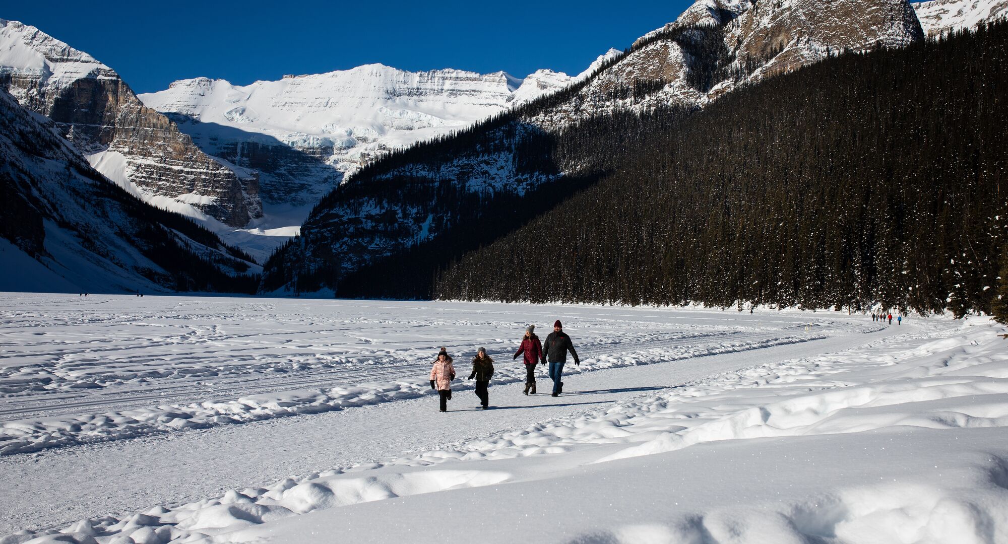 A family hiking along the Lake Louise lakeshore trail in the winter