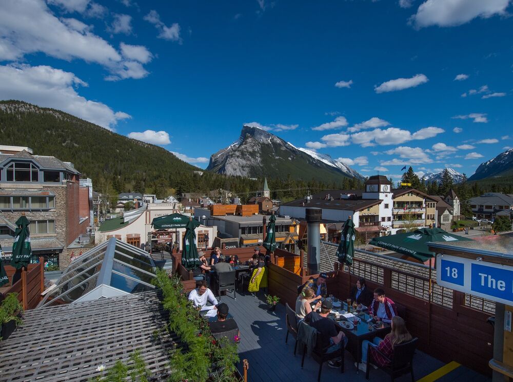 People dining on the rooftop patio at the Elk & Oarsman restaurant in Banff National Park with Rundle Mountain in the background