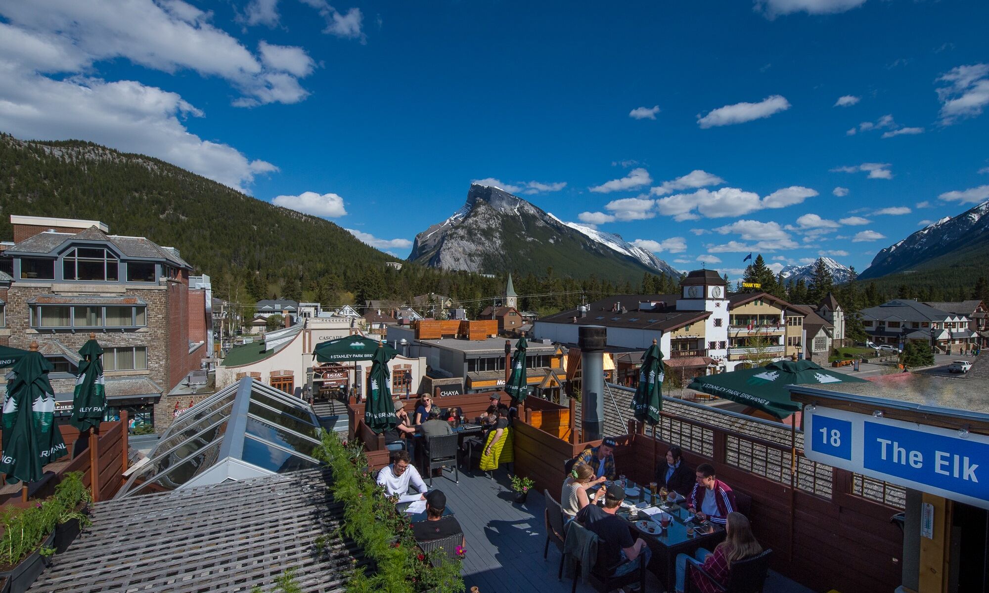 People dining on the rooftop patio at the Elk & Oarsman restaurant in Banff National Park with Rundle Mountain in the background