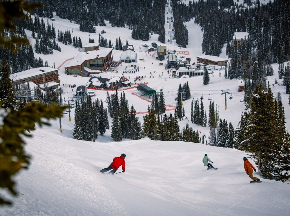 A skier and two snowboarders head down hill towards base camp at Sunshine Village.