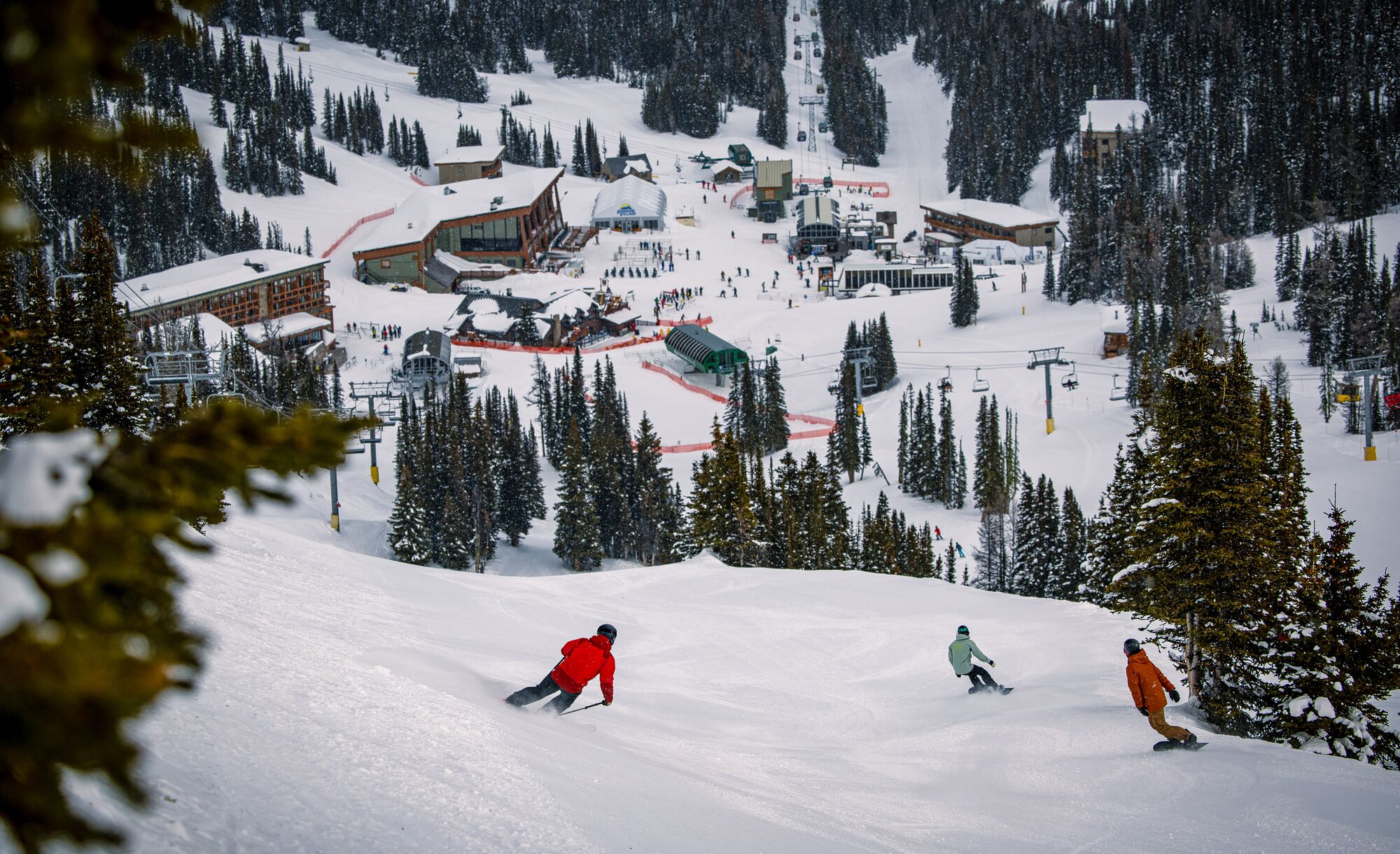 A skier and two snowboarders head down hill towards base camp at Sunshine Village.