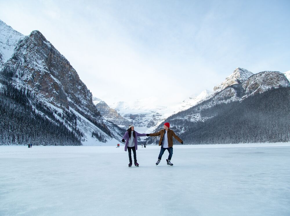 A couple skate on a frozen Lake Louise with mountains behind them in Banff National Park.