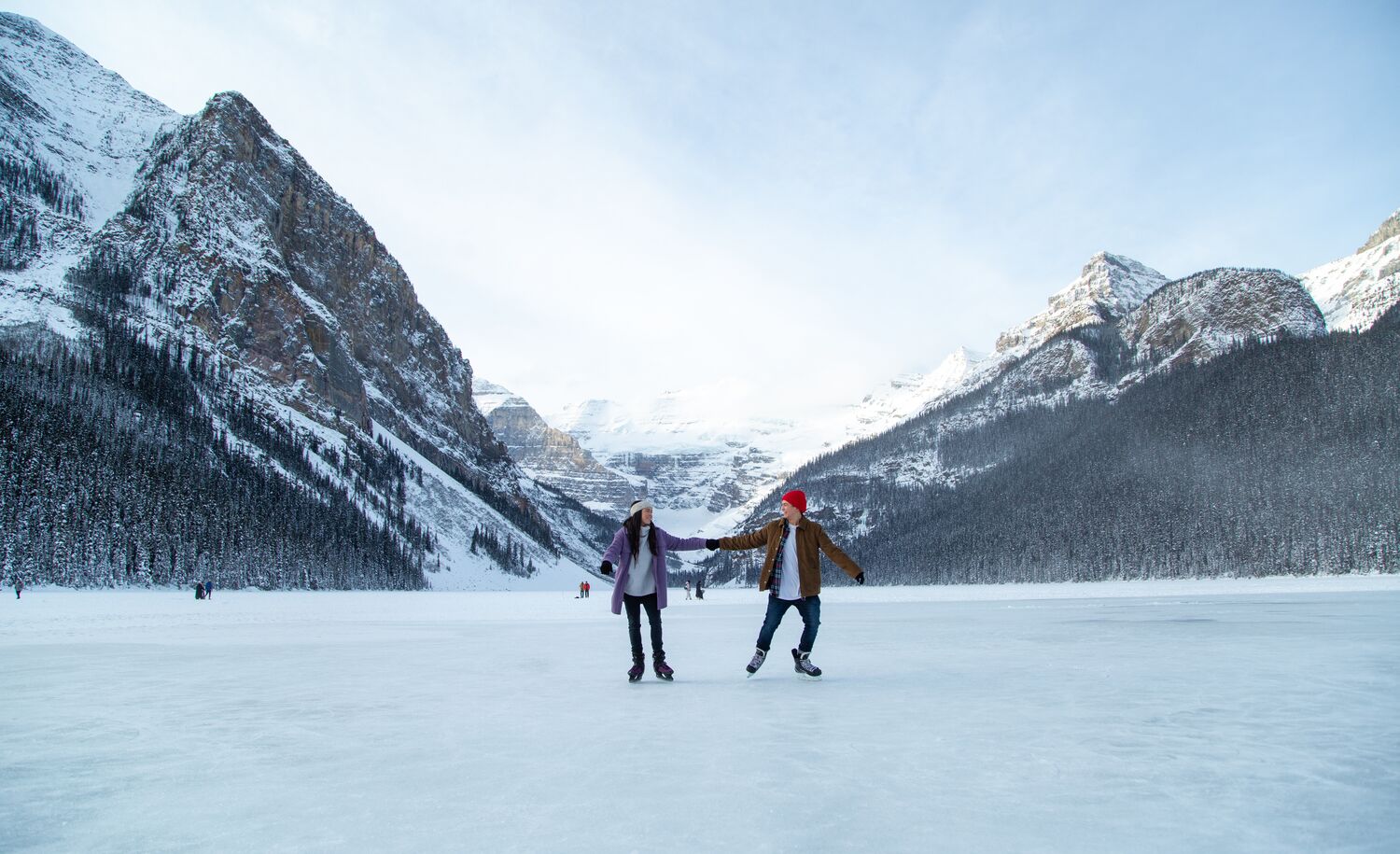 A couple skate on a frozen Lake Louise with mountains behind them in Banff National Park.