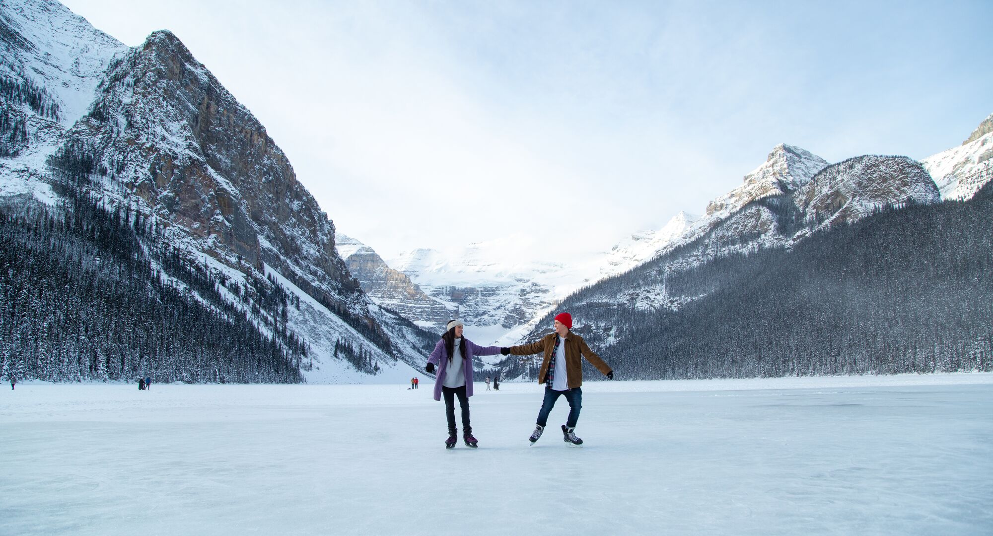 A couple skate on a frozen Lake Louise with mountains behind them in Banff National Park.