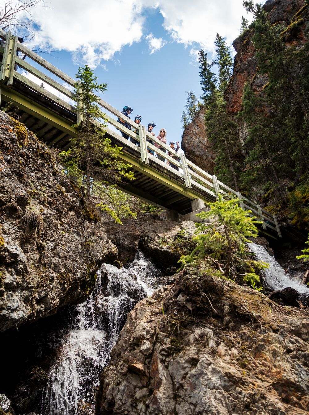 People stand on a bridge at Sundance Canyon with a waterfall underneath of them in Banff National Park.