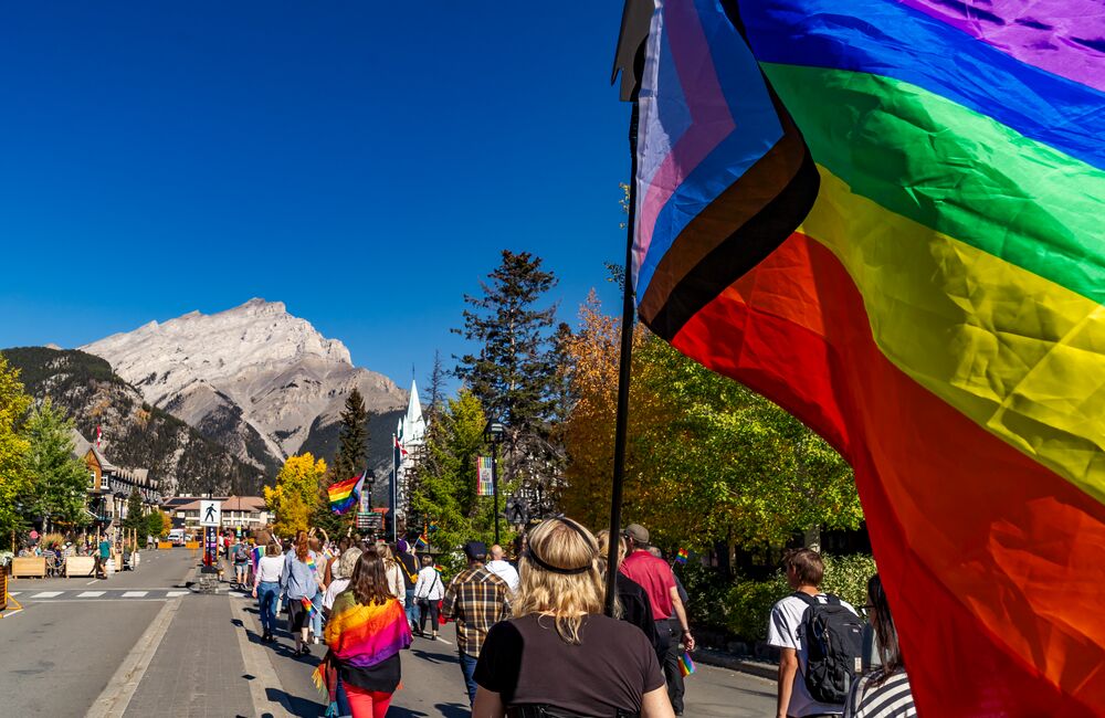 A pride flag in the Banff Pride parade on Banff Ave with Cascade Mountain in the background.