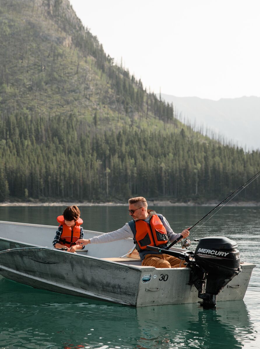A father and son fish off a motor boat in the blue water of Lake Minnewanka