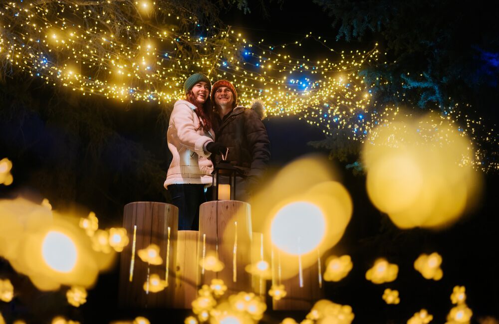 A couple walking through a lit up Cascade of Times Garden for In Search of Christmas Spirit in Banff