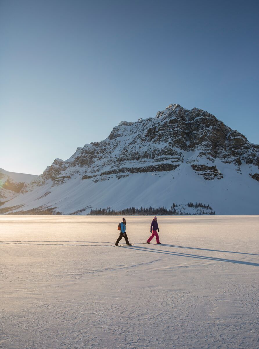 Two people snowshoeing across Bow Lake in the winter